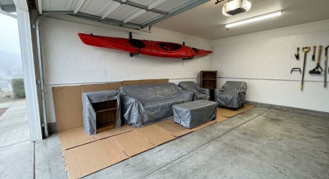 Covered sofa, chairs and shelves stored on cardboard in a garage