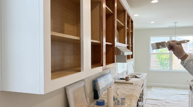 Painter brushing white paint on upper cabinet frames