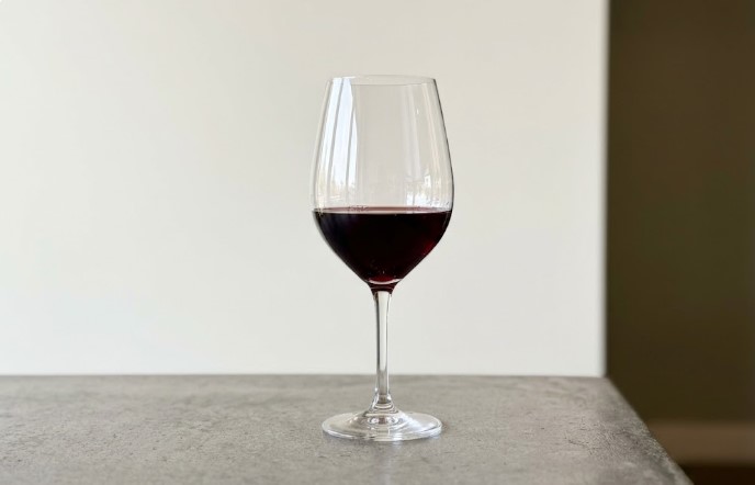 Glass of red wine on a gray stone counter in front of a plain off-white wall